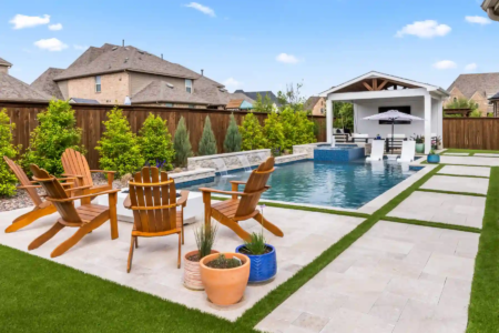 Wooden chairs near a pool and outdoor kitchen